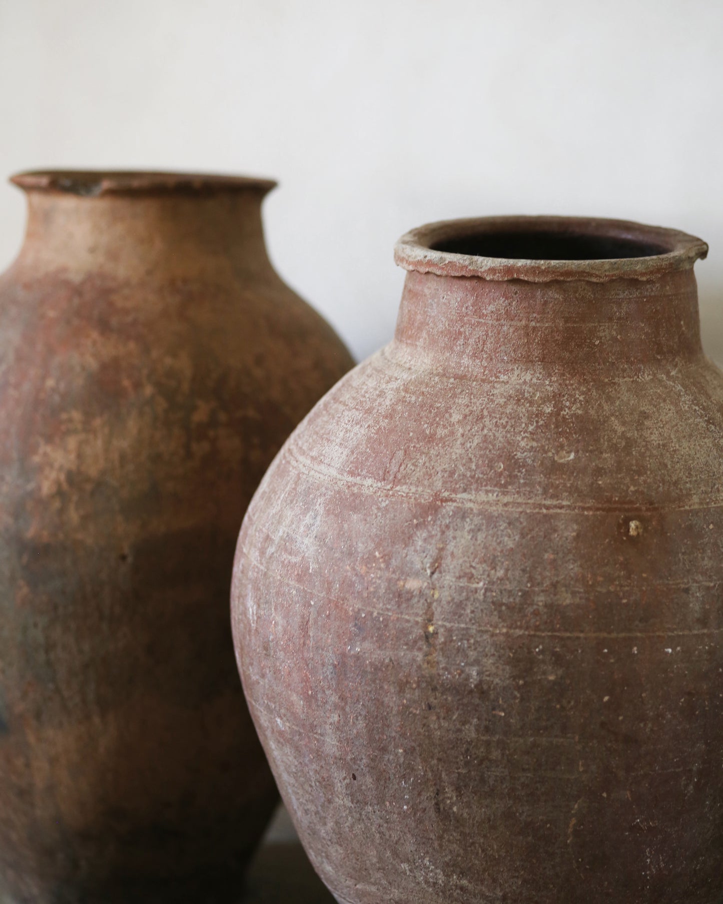 Two rustic clay pots with lots of aged patina on a plain background