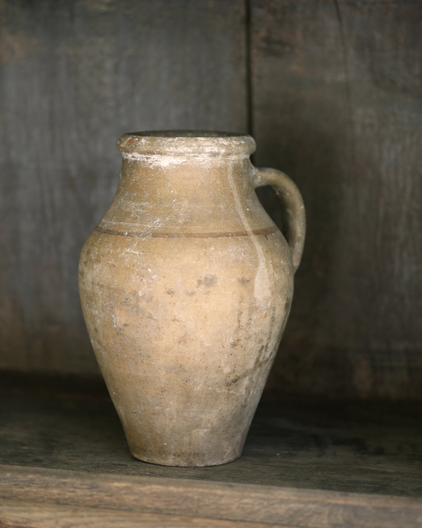 Vintage terracotta pot with handle on a wooden surface with a rustic background