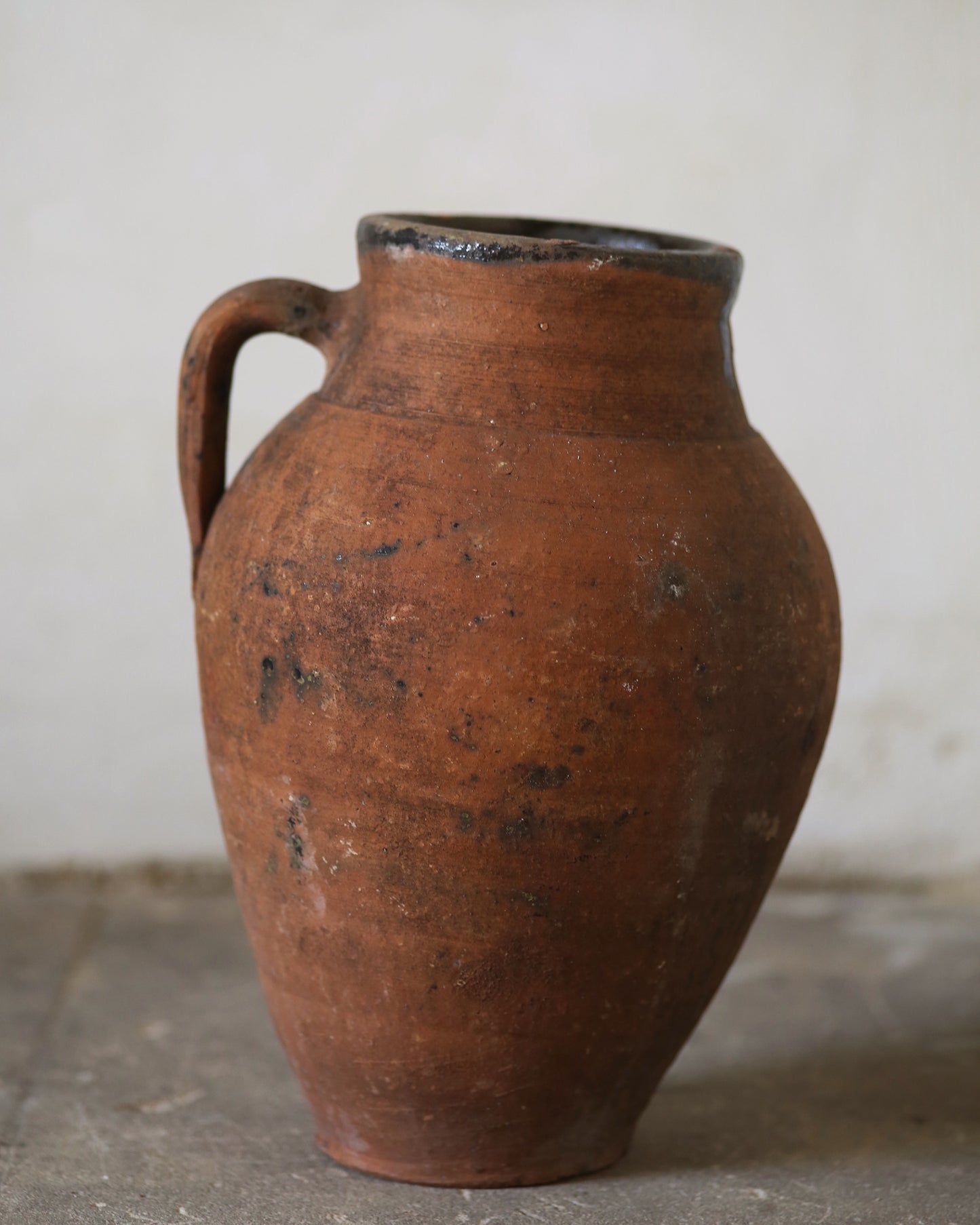 Brown ceramic jar with a handle on a gray surface and light gray background