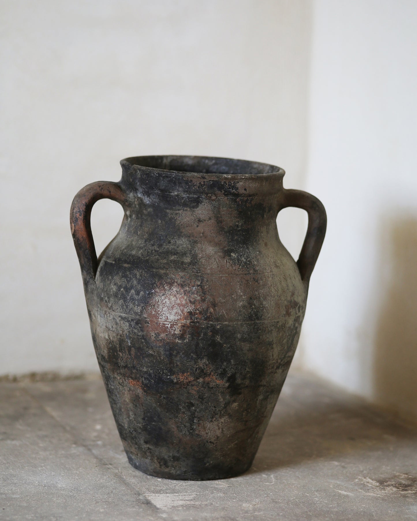 Ancient terracotta vase with two handles on a stone surface.