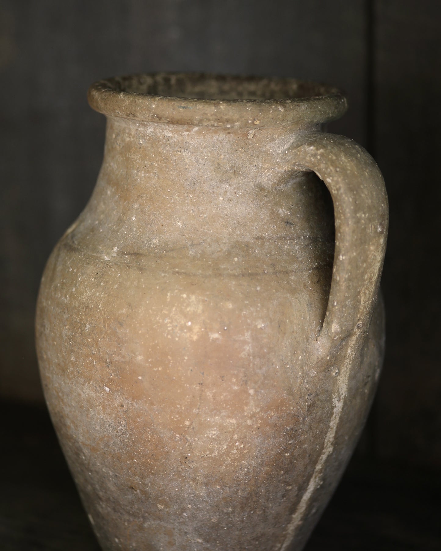 Ancient terracotta jar with a handle on a dark background