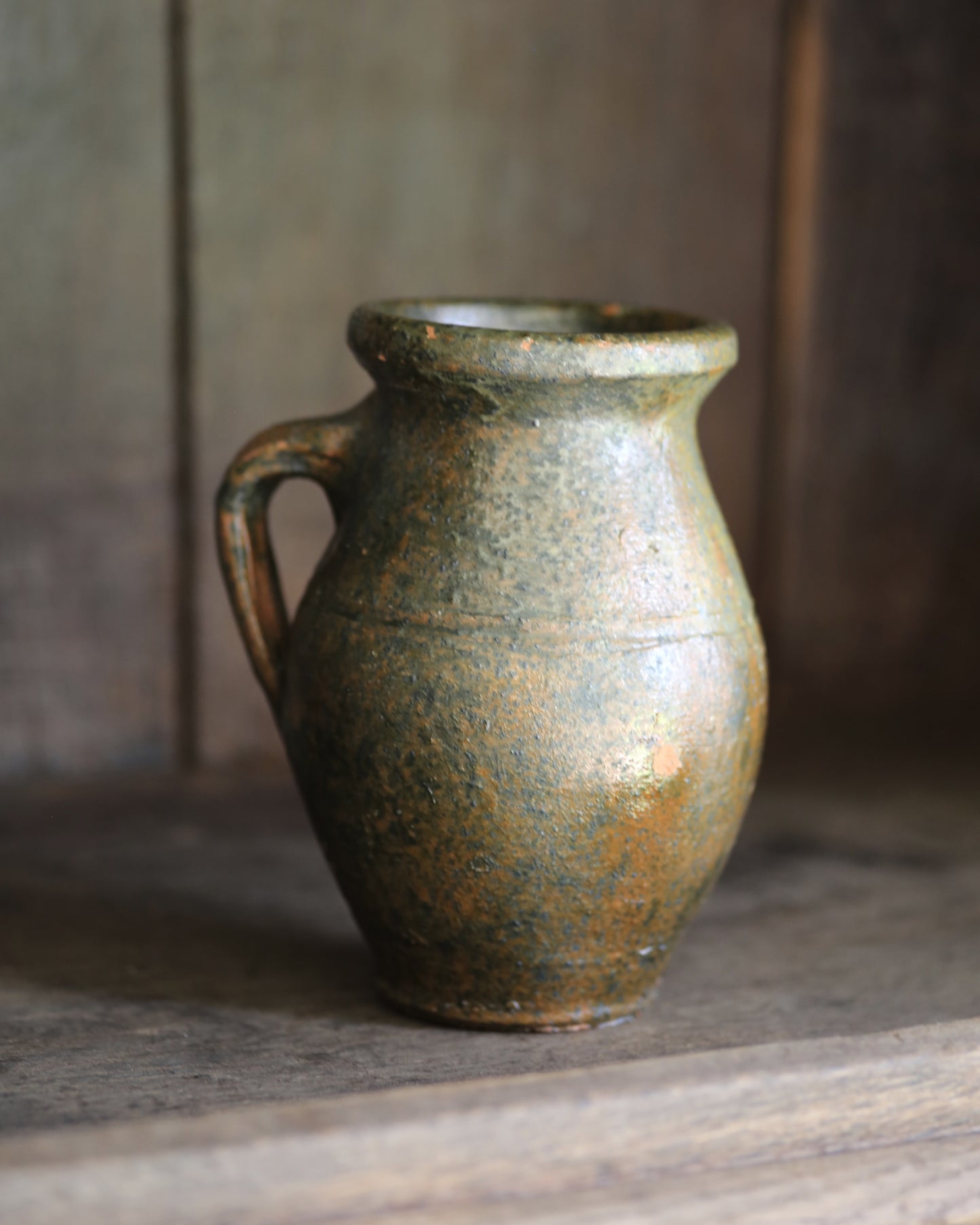 Vintage green glaze small pitcher pot on wooden shelving.