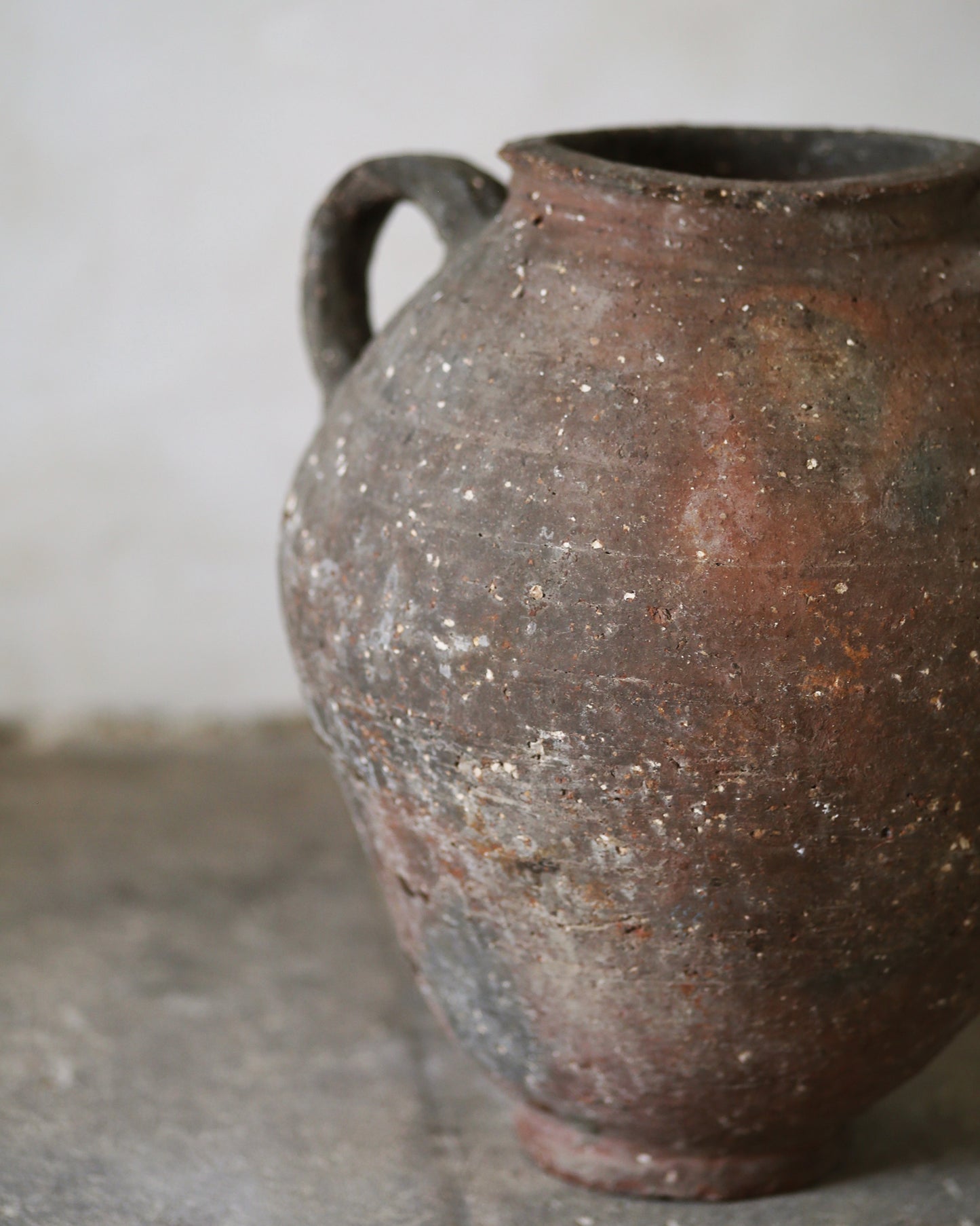 Brown ceramic urn with a handle sat on a gray flagstones