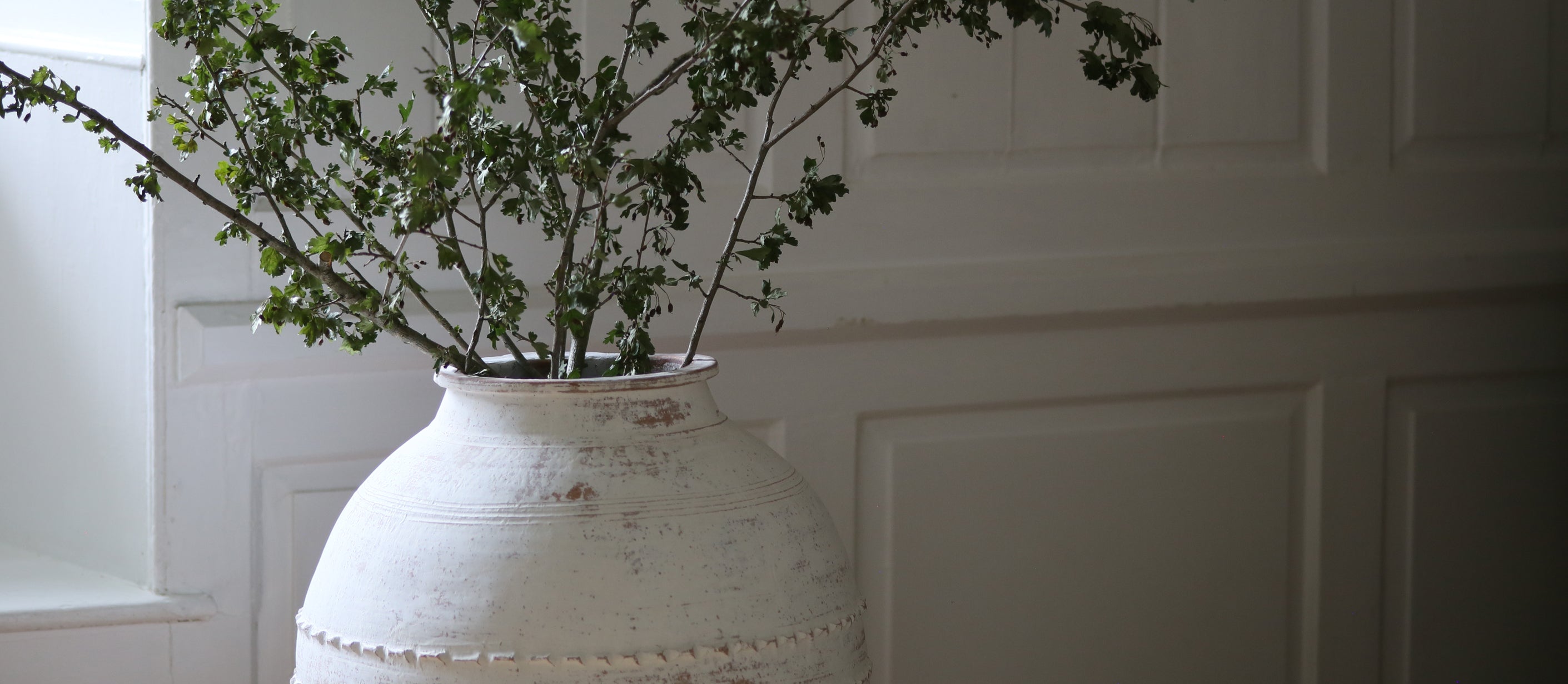 Statement floor standing white urn with handmade ribbed detail styled with branches from the garden