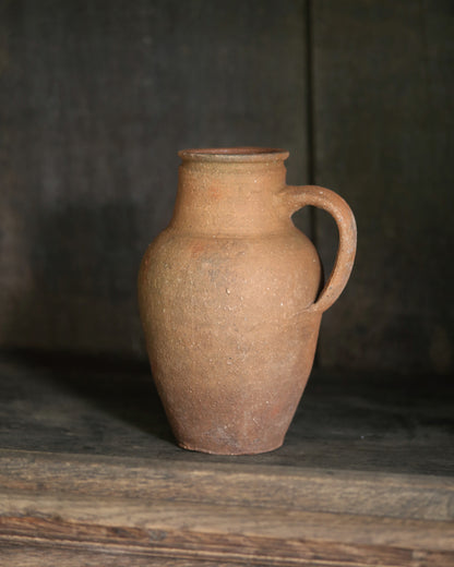 Brown terracotta pitcher pot on a wooden surface with a dark background