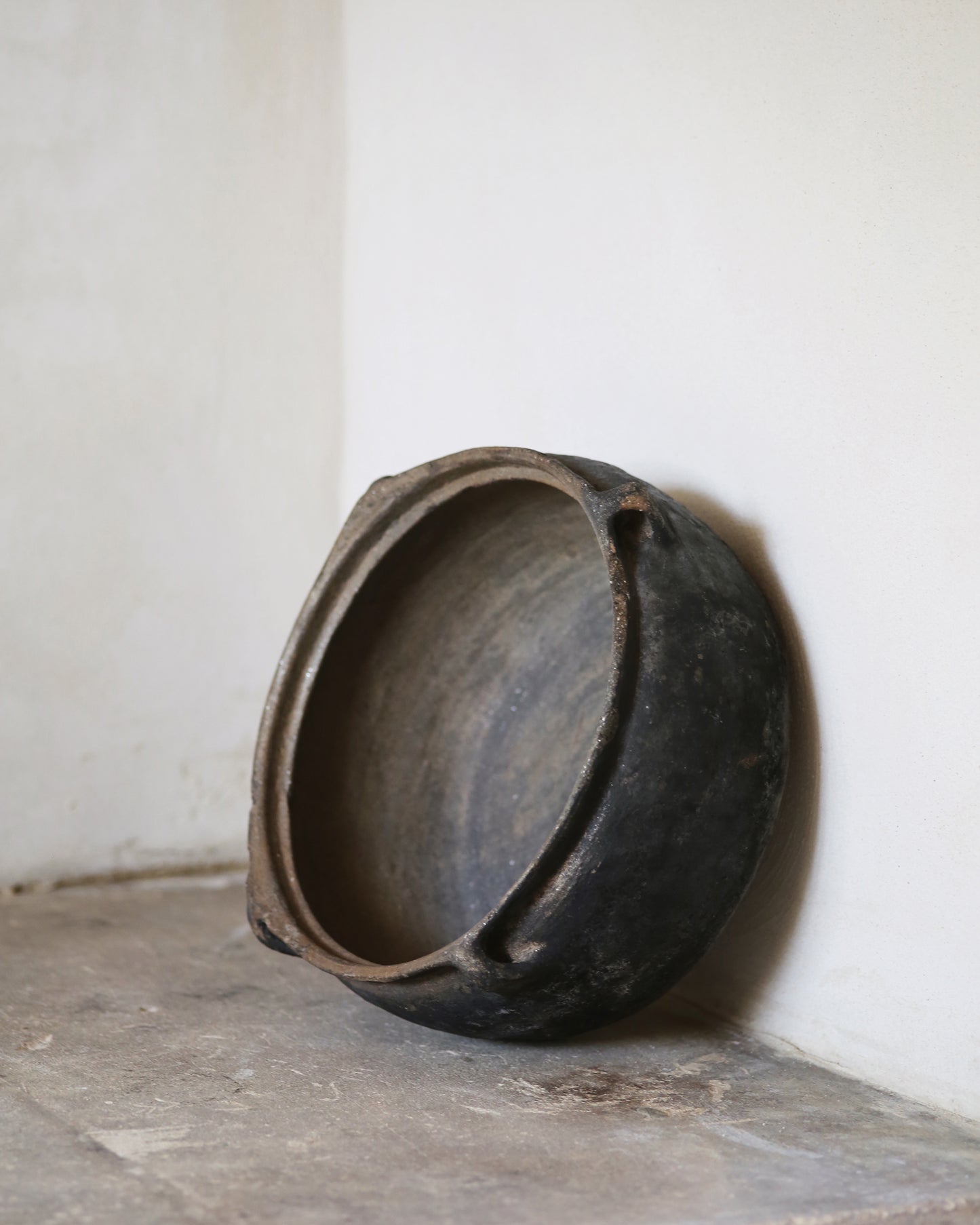 Black clay bowl on a flagstone surface with a white wall background