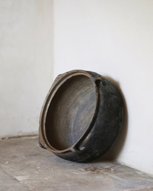 Black clay bowl on a flagstone surface with a white wall background