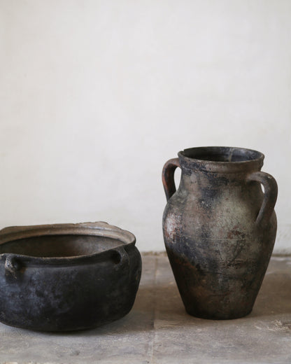 Two ancient-looking black pots on a stone surface with a white background