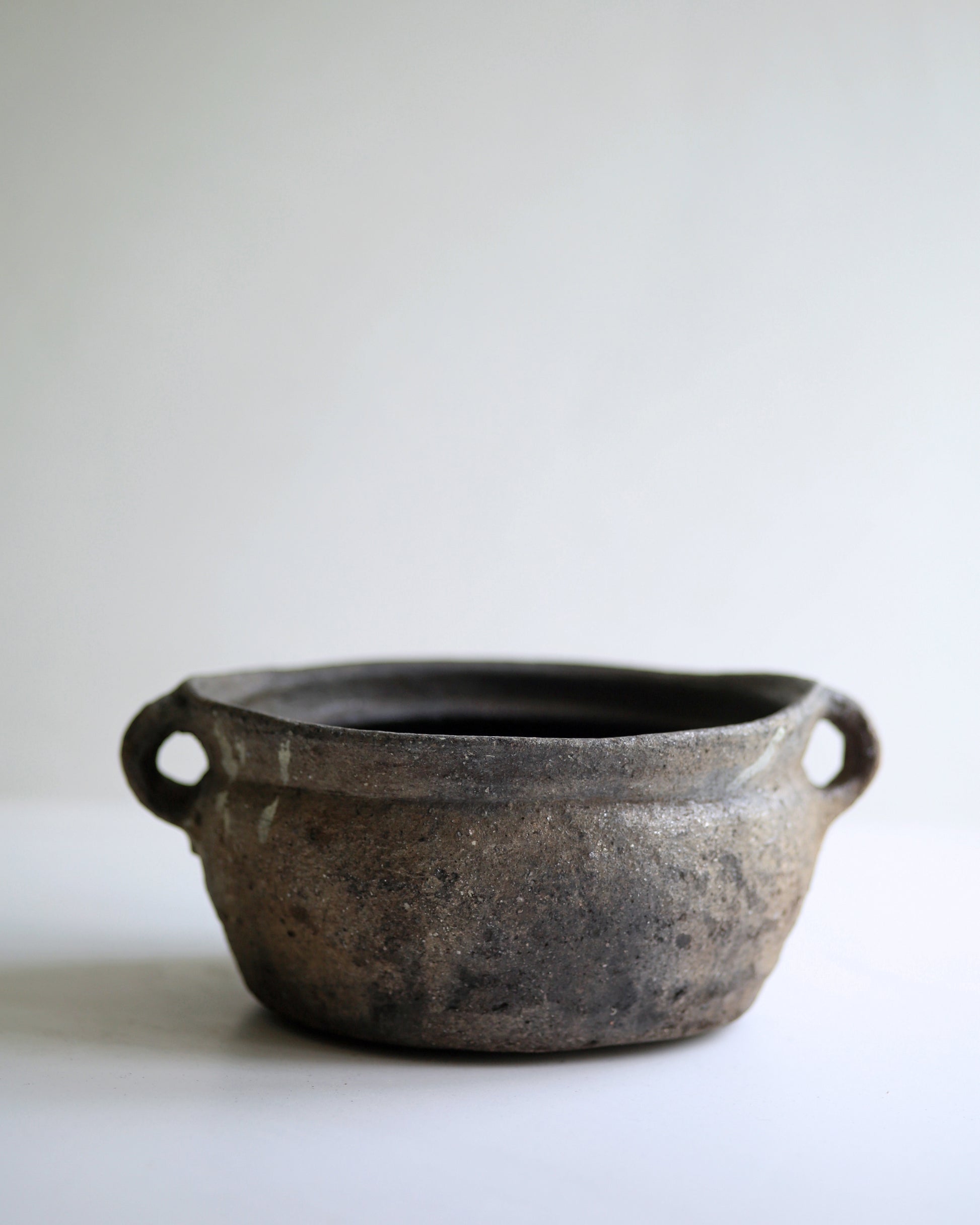 Dark black clay bowl with two small handles to use as a decorative display piece