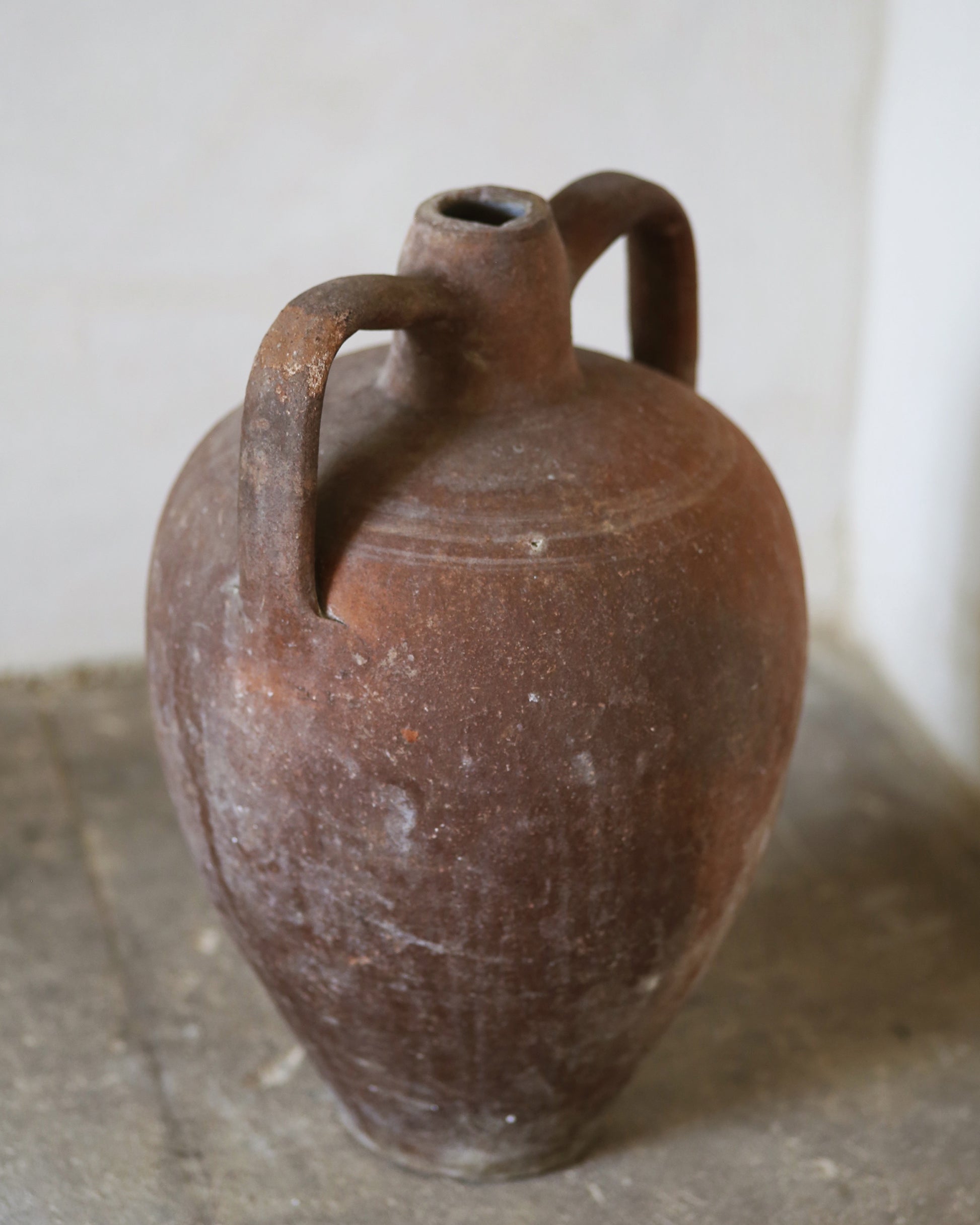 Brown-red ceramic jar with two handles on a concrete floor.