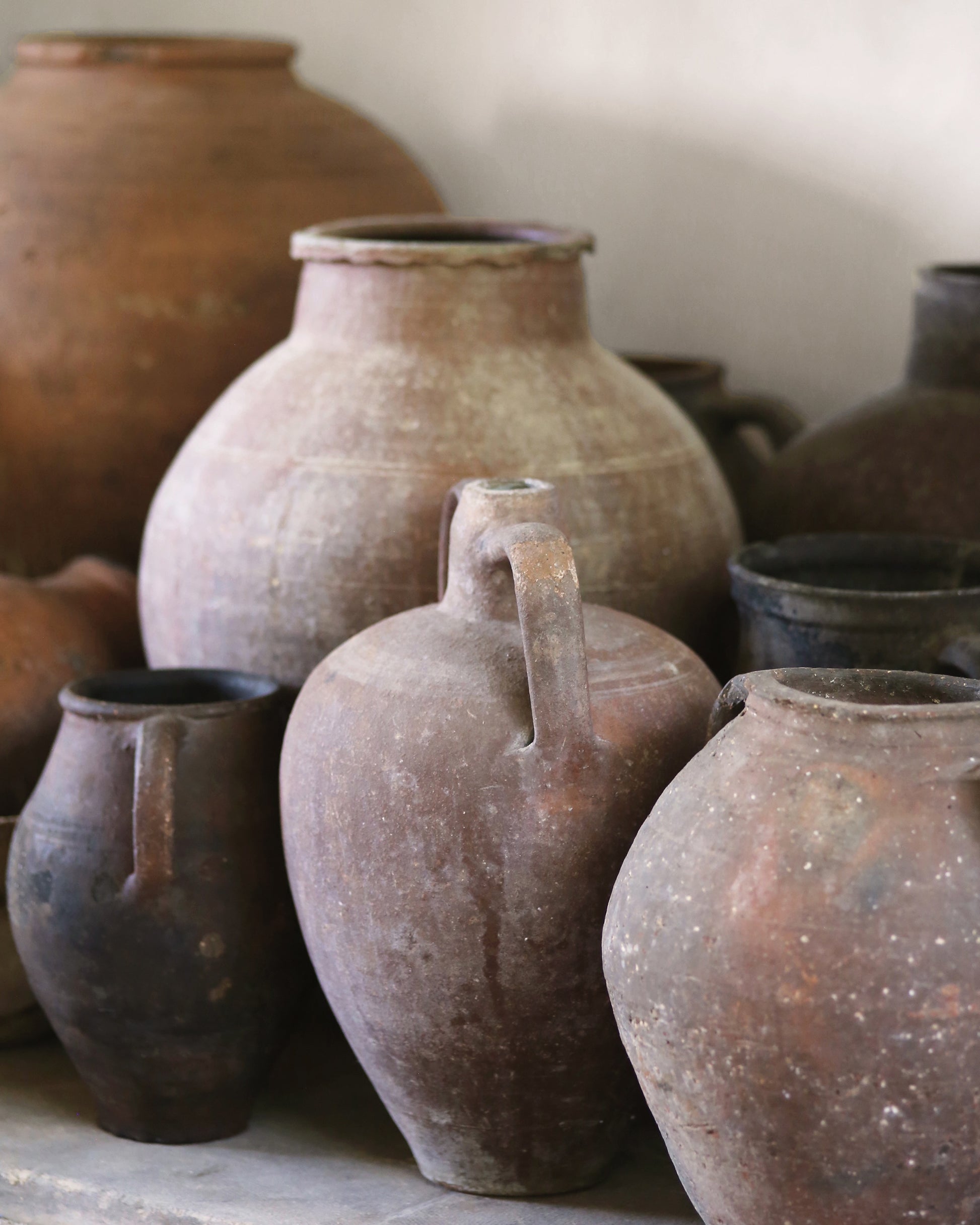 Collection of rustic antique Turkish clay pots with handles on a stone surface.