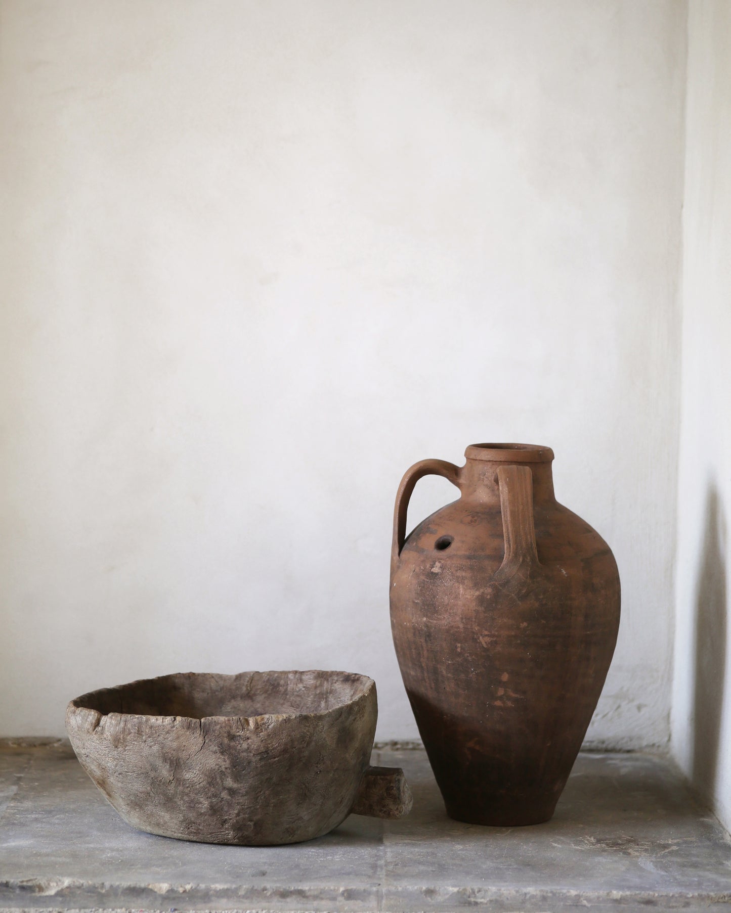 Antique amphora and vintage wooden carved bowl sat on a fire hearth against a lime plastered wall