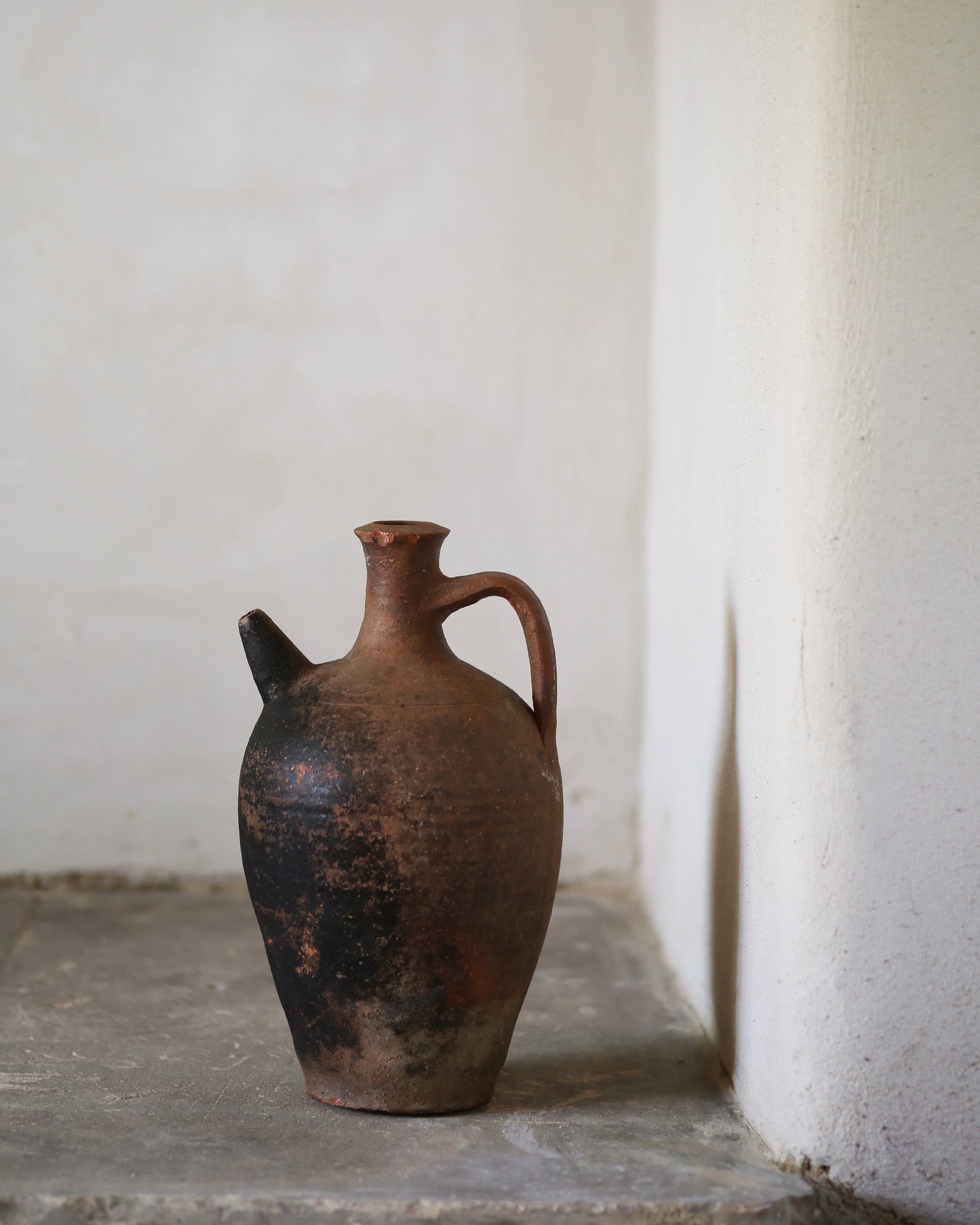 Vintage terracotta jug on a stone surface with a white wall background