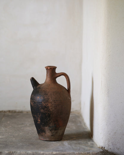 Vintage terracotta jug on a stone surface with a white wall background