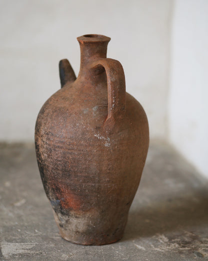Brown ceramic jug with a handle on a gray surface against a white wall