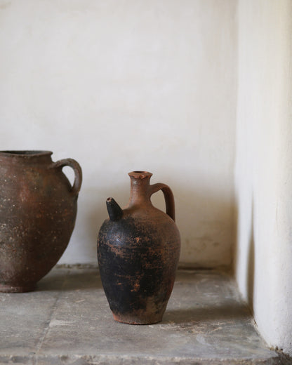 Two antique Turkish rustic clay pots on a stone floor with a white wall background