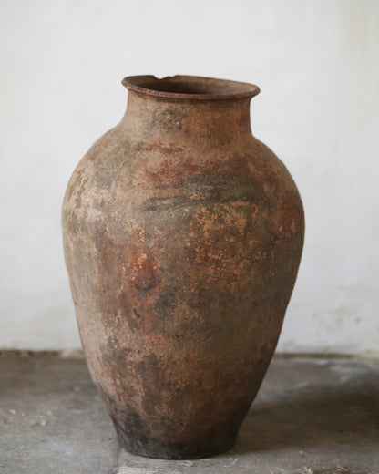 Rust-coloured antique ceramic jar on a gray flagstone floor with a white background