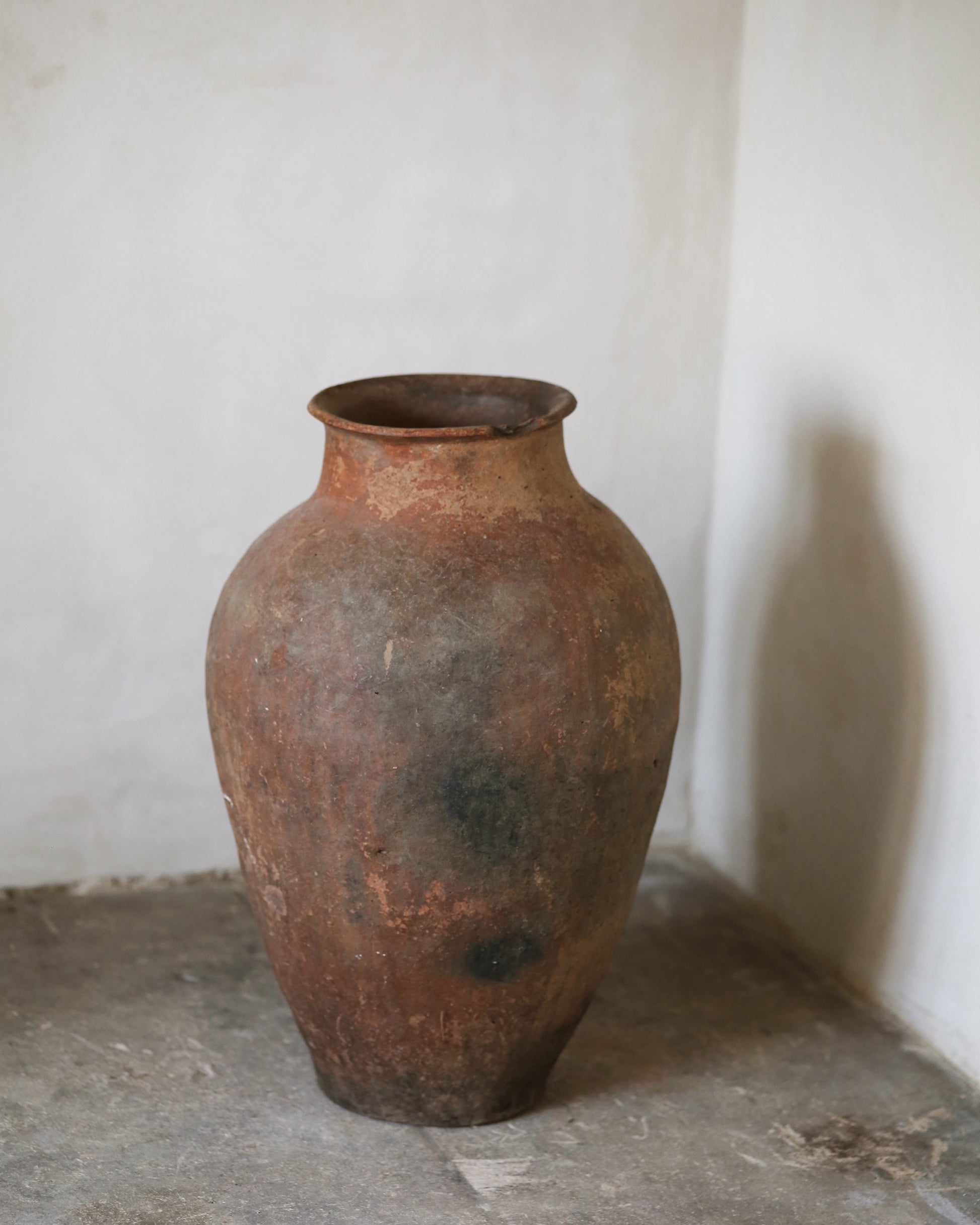 Rust-coloured terracotta pot on a stone surface with a white wall background