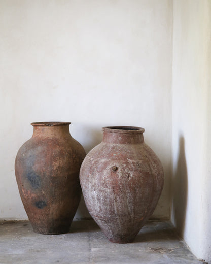 Two rustic wabi-sabi old clay pots against a plain wall.