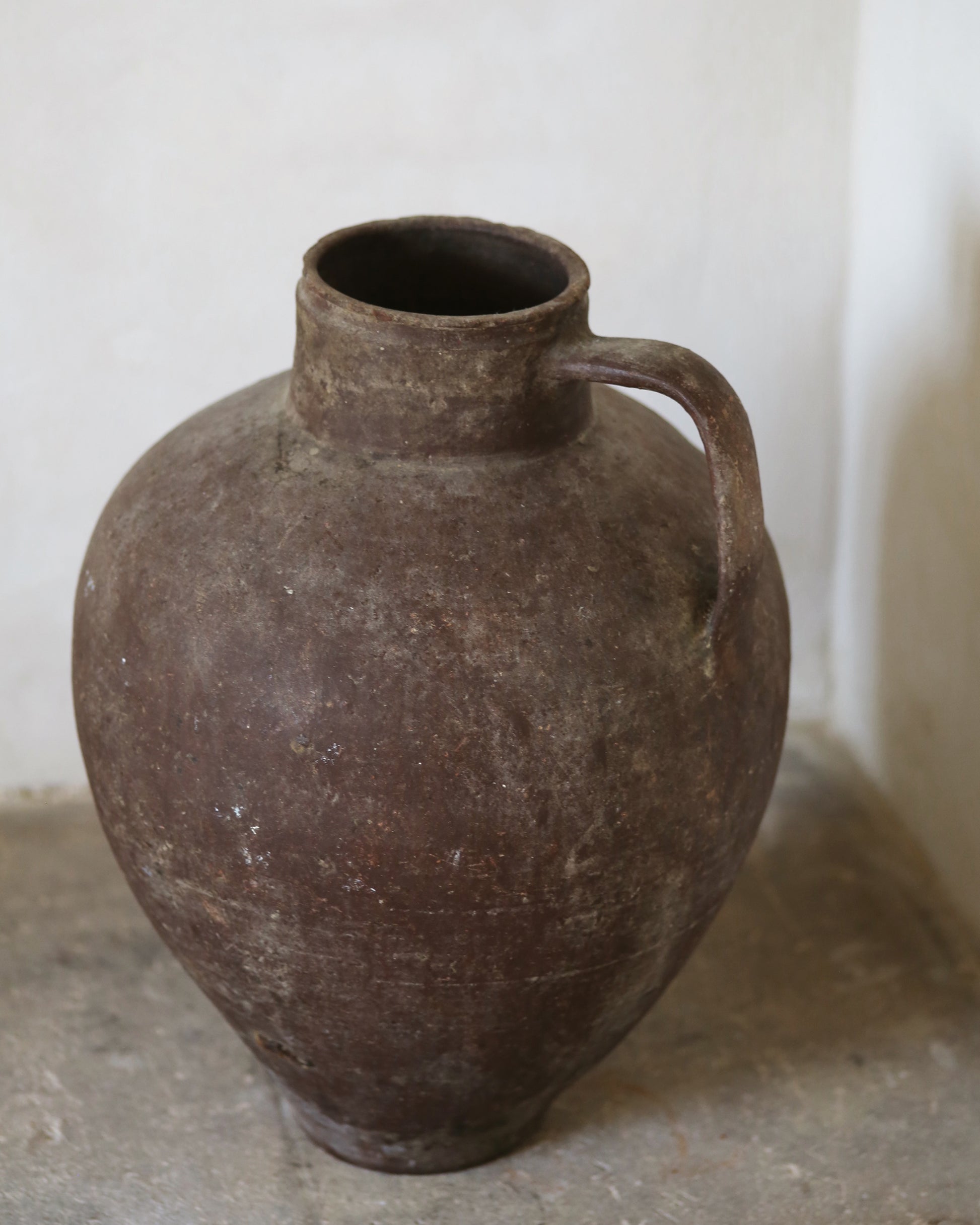 Brown ceramic jug on a concrete floor with a white wall background