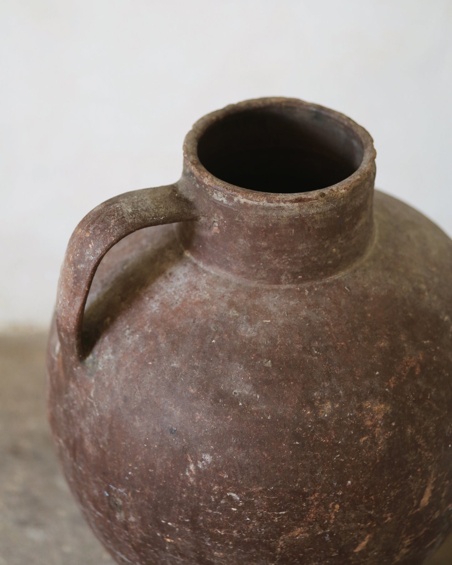 Brown terracotta olive jar with a handle on a light background