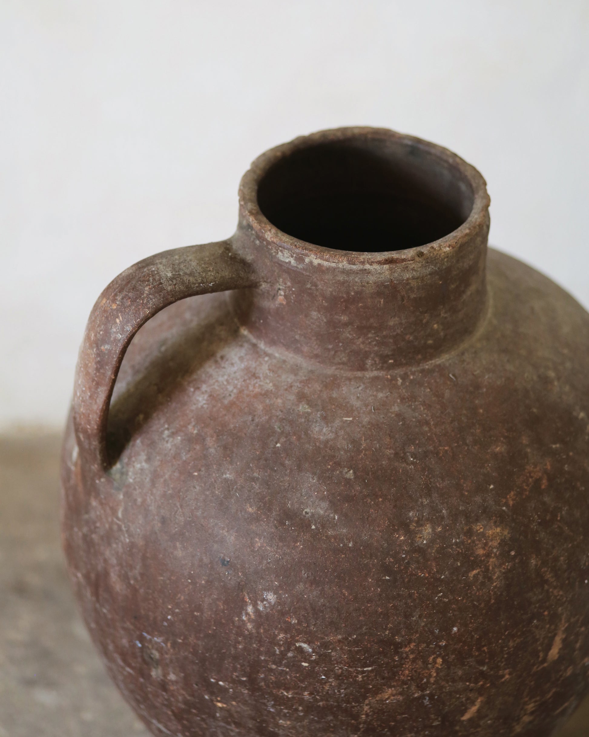 Brown terracotta olive jar with a handle on a light background
