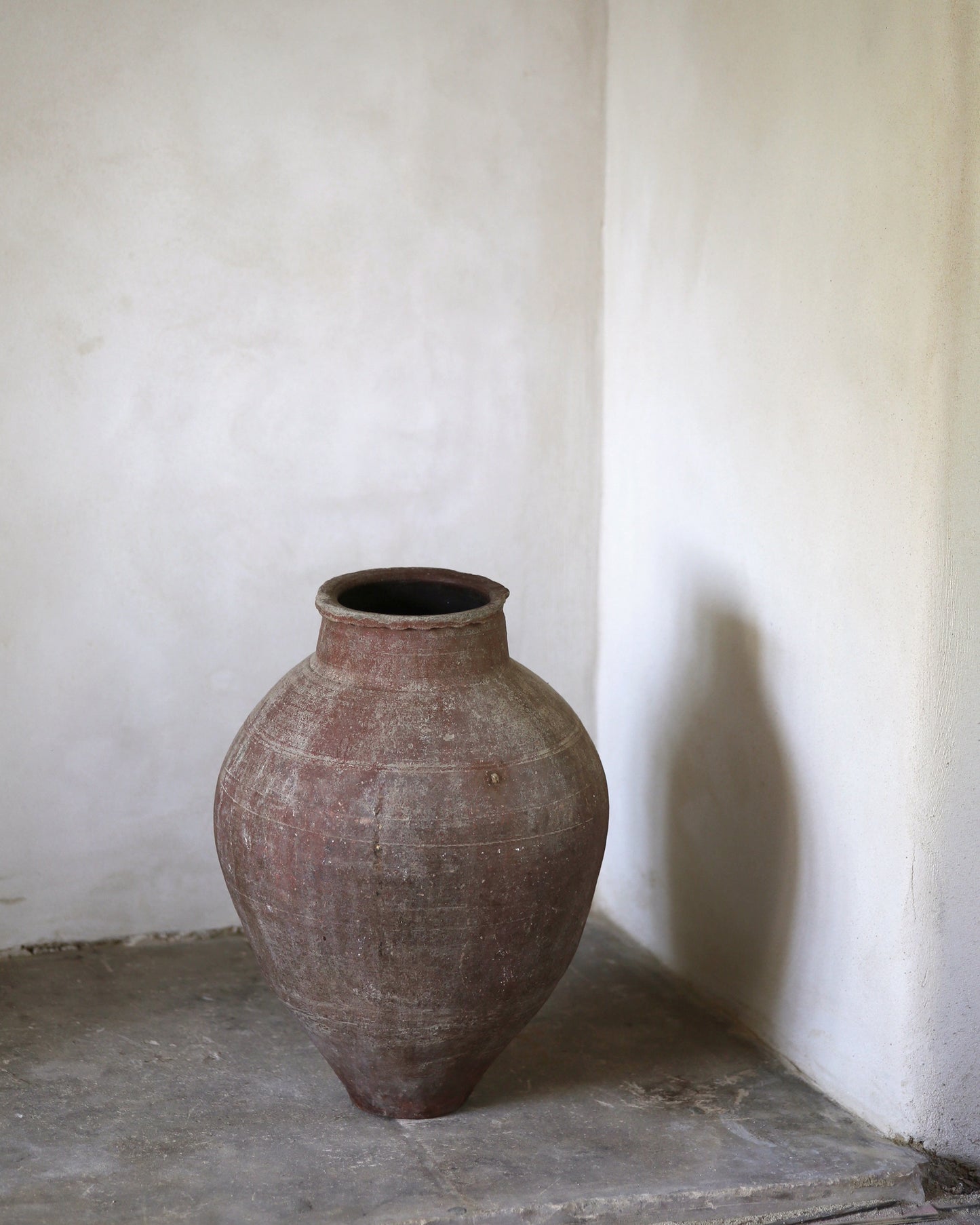 Vintage terracotta pot on a stone surface with a white wall background