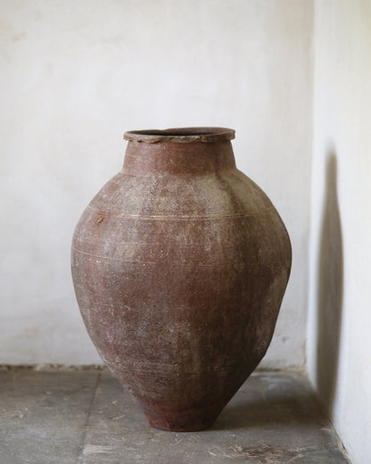 Large floor standing brown ceramic vase against a plain white wall