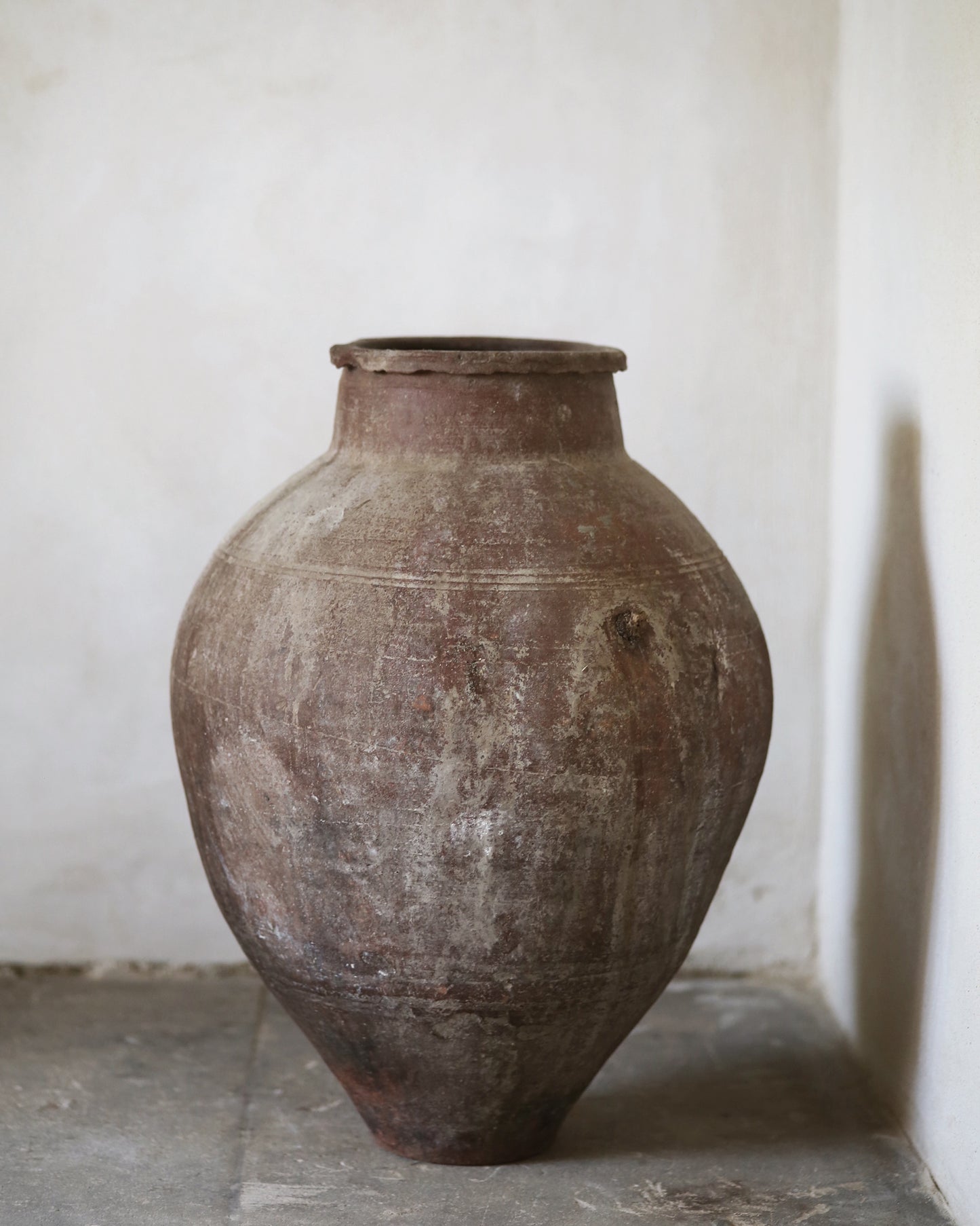 Large brown ceramic jar on old gray flagstones with a white wall background