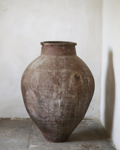 Large brown ceramic jar on old gray flagstones with a white wall background
