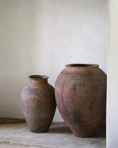 Two rustic clay pots on a stone surface with a plain wall background