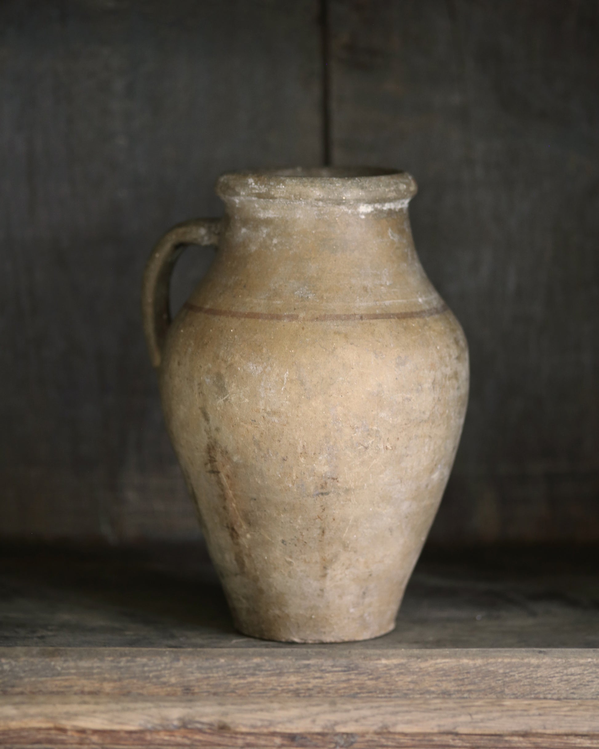 Vintage mediterranean clay jar with a handle on a wooden surface against a dark background