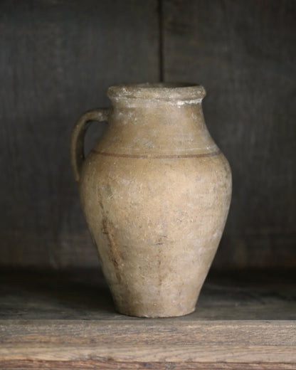 Vintage mediterranean clay jar with a handle on a wooden surface against a dark background