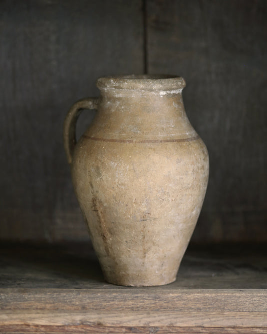 Vintage mediterranean clay jar with a handle on a wooden surface against a dark background