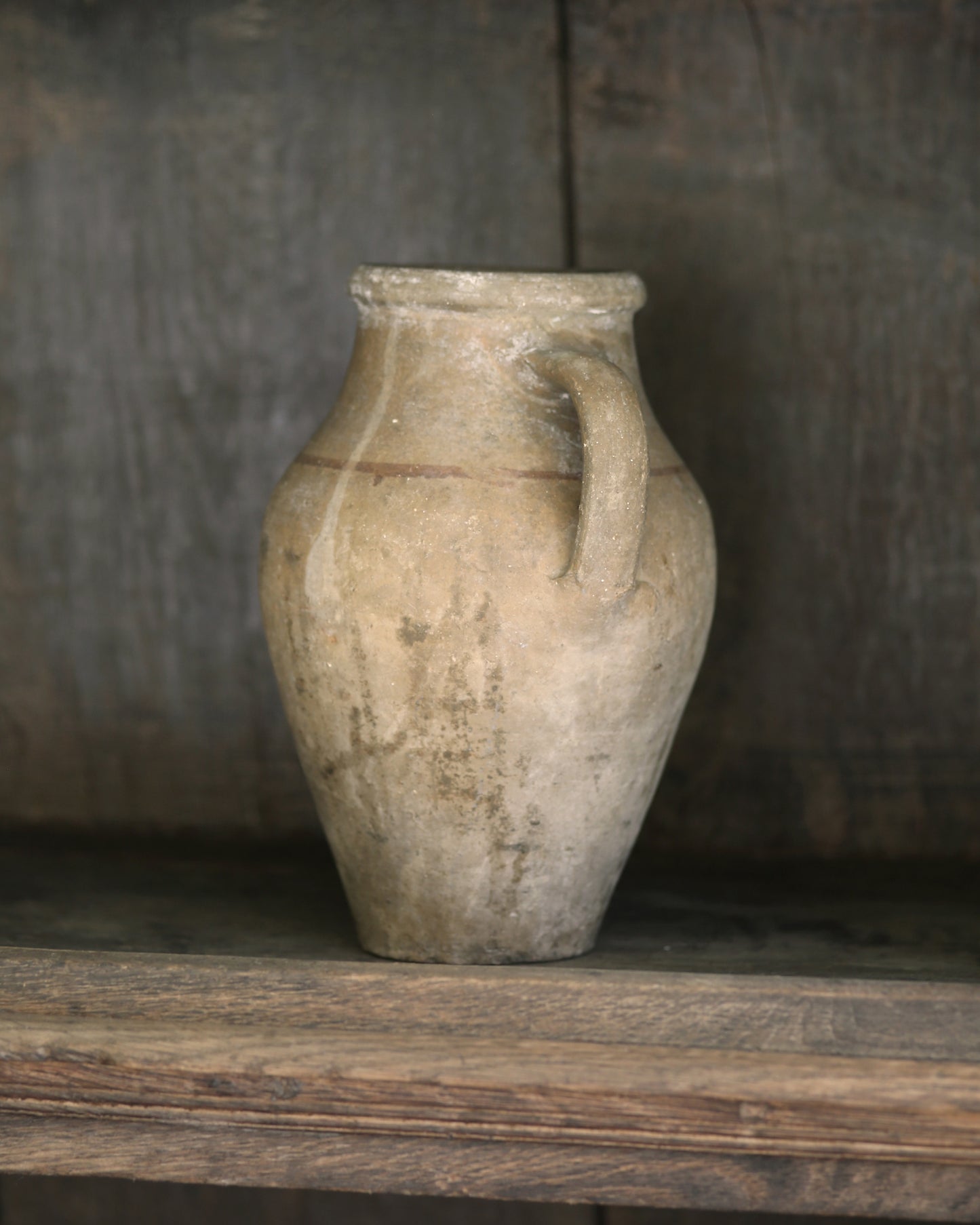 Vintage-style ceramic jar with a handle on a wooden shelf against a rustic background