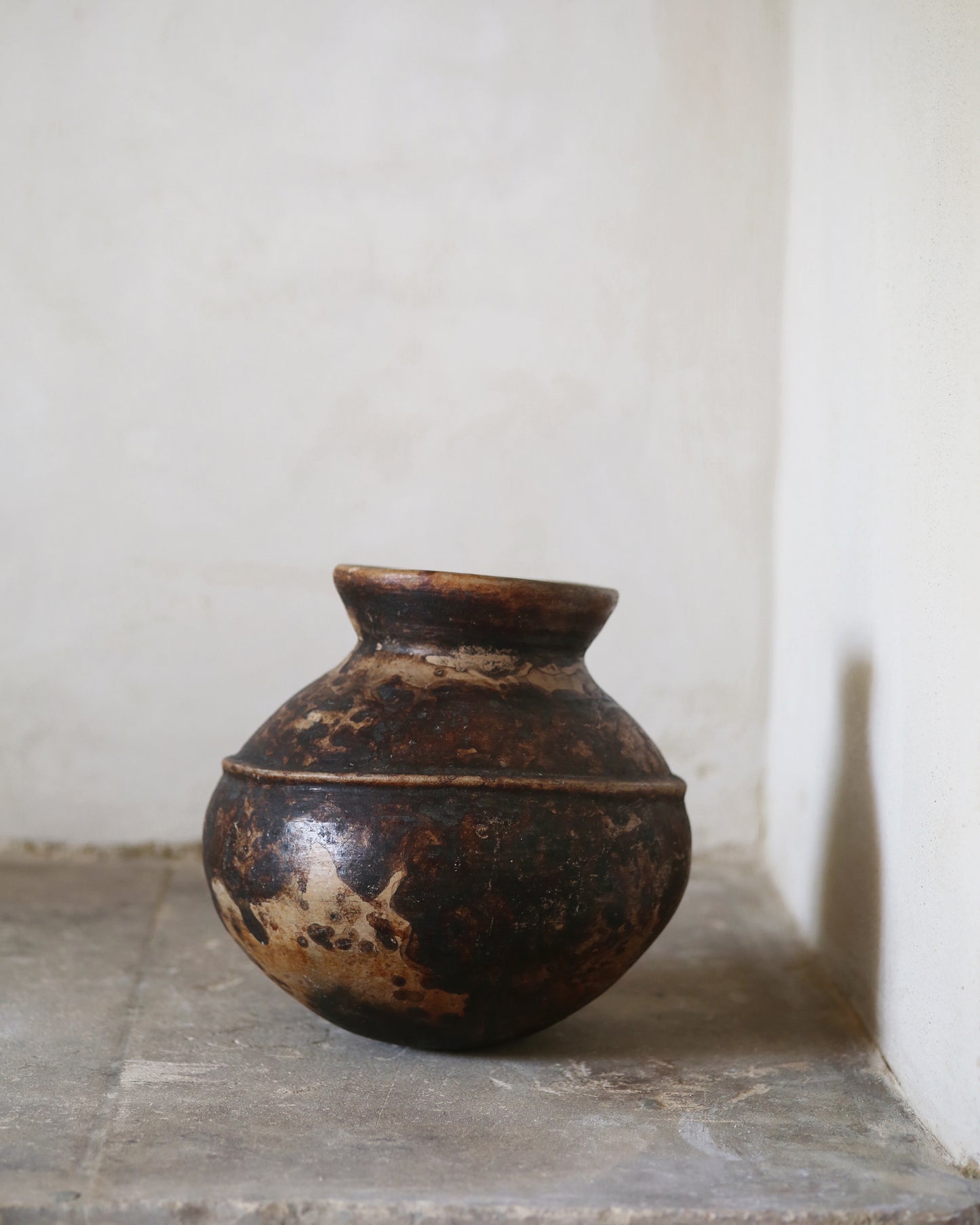 Rich brown ceramic Nigerian water pot against flagstone floor