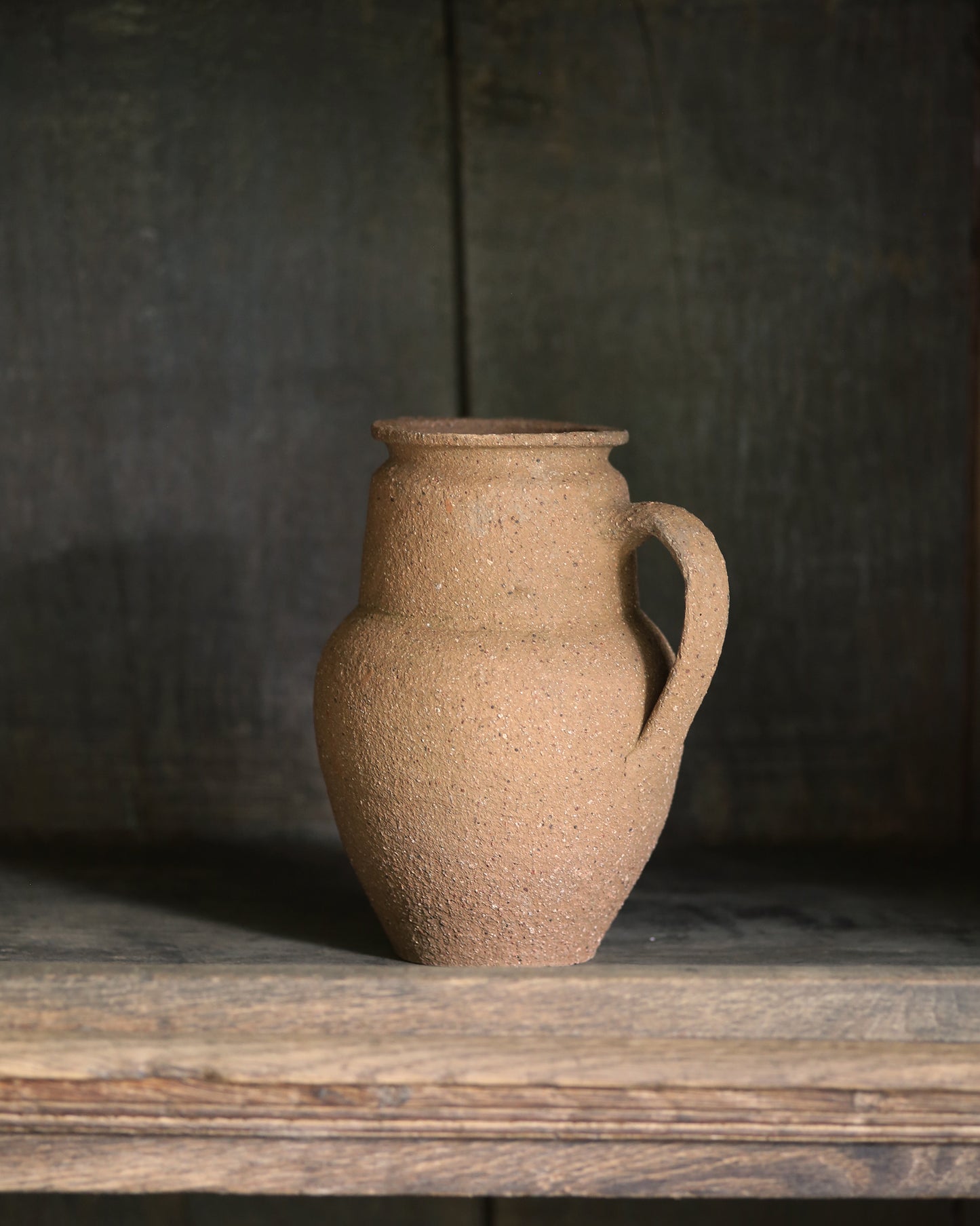 Vintage terracotta pitcher pot on a wooden surface with a dark background