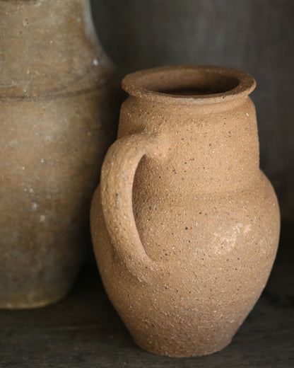 Two brown ceramic pots with handles on a dark background