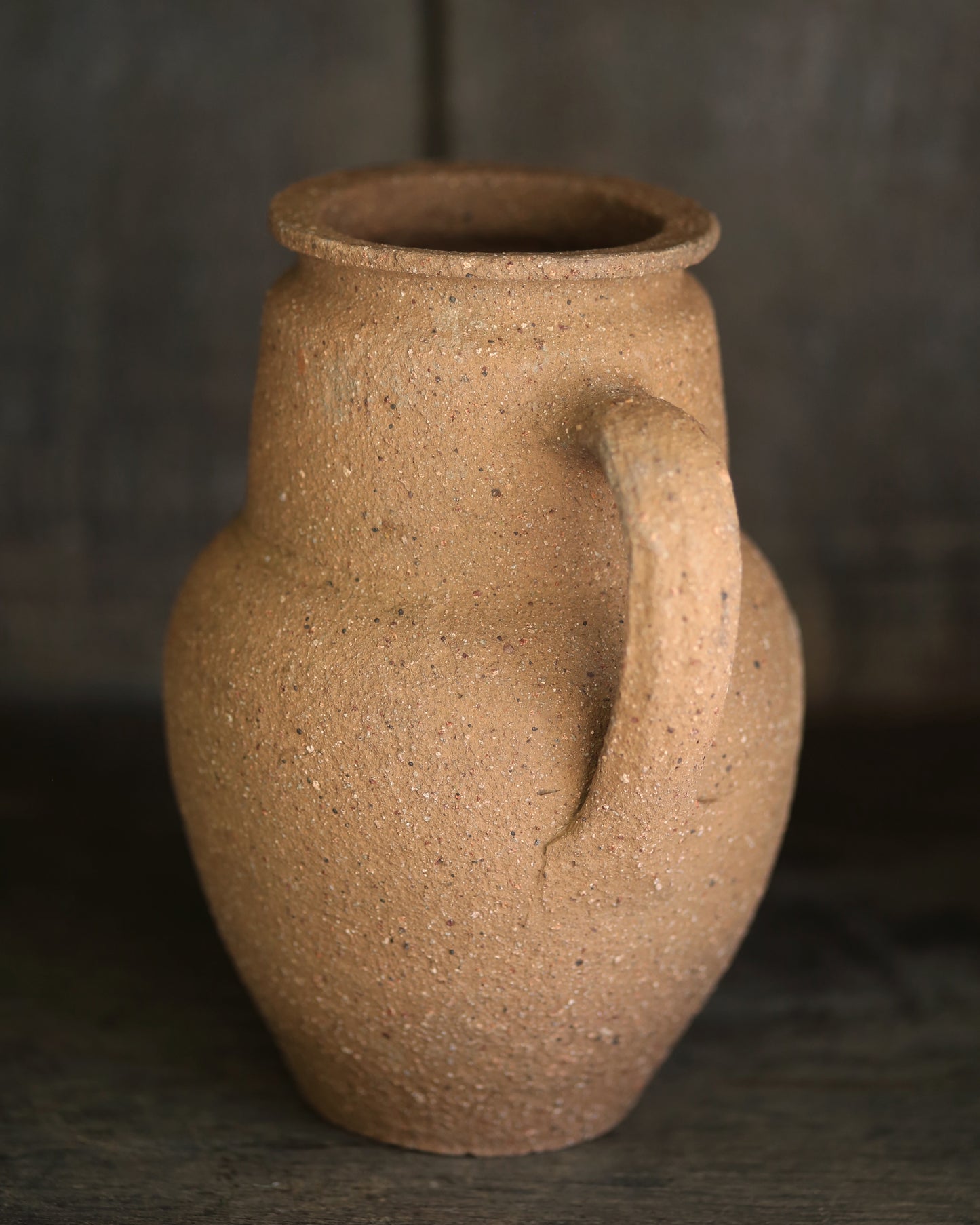 Brown textured terracotta pottery piece on a dark shelf
