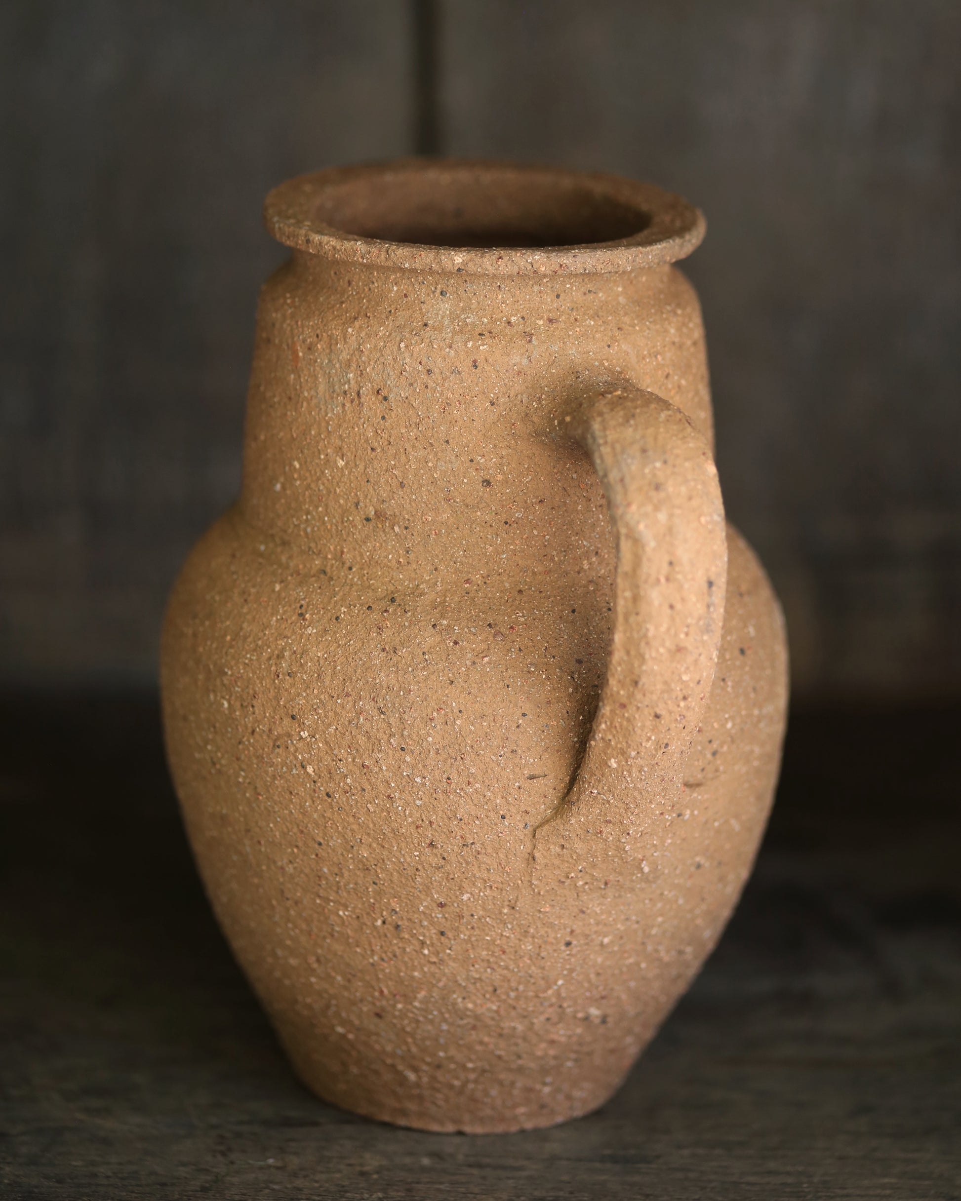 Brown textured terracotta pottery piece on a dark shelf