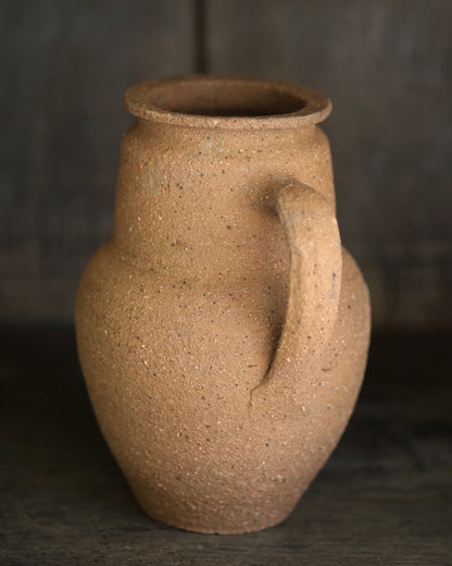 Brown textured terracotta pottery piece on a dark shelf
