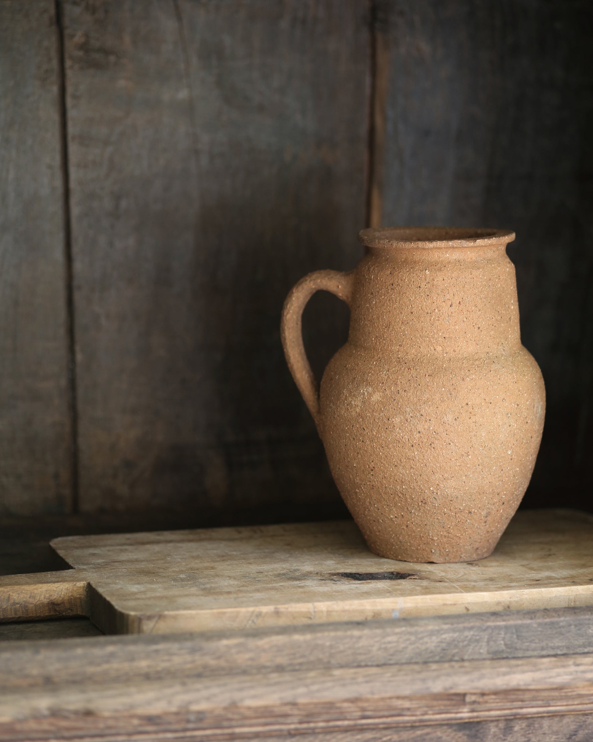 Terracotta pitcher pot on a vintage wooden breadboard in an antique bookcase