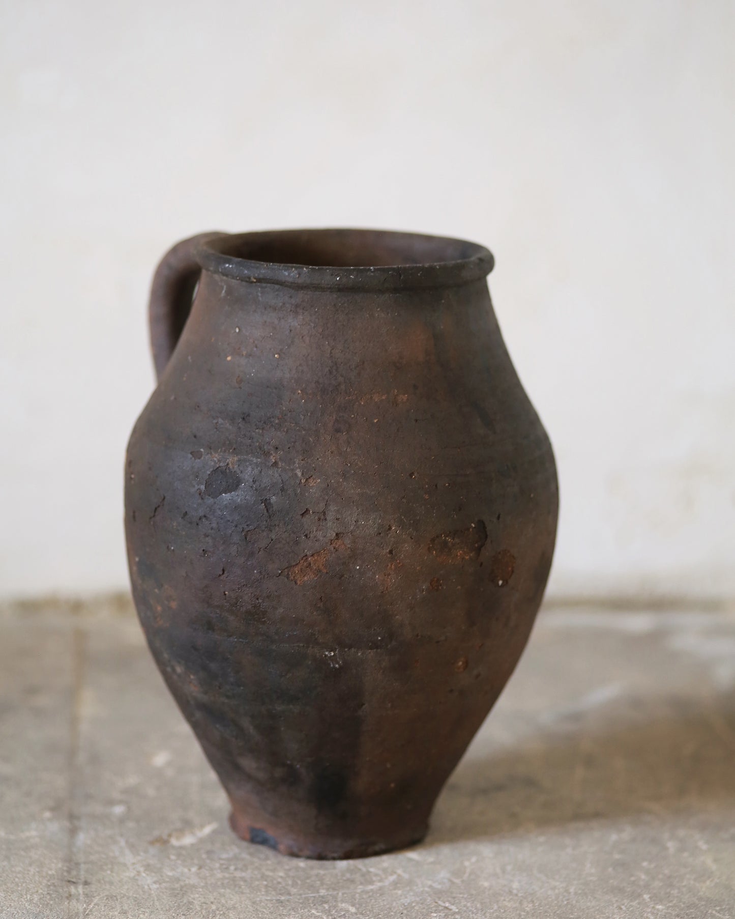 Brown ceramic jar on a concrete floor with a white wall background