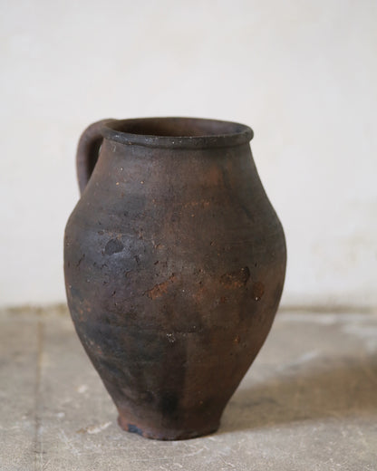 Brown ceramic jar on a concrete floor with a white wall background