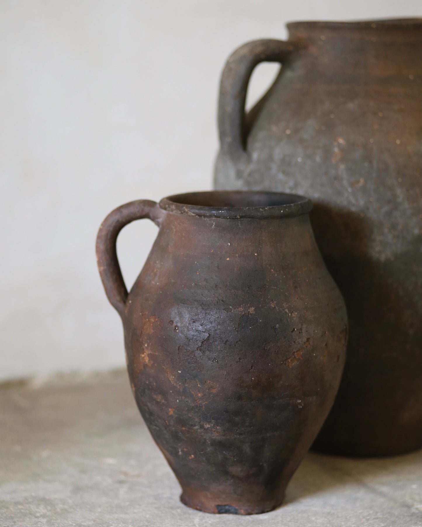 Two rustic clay pots on a stone surface with a neutral background