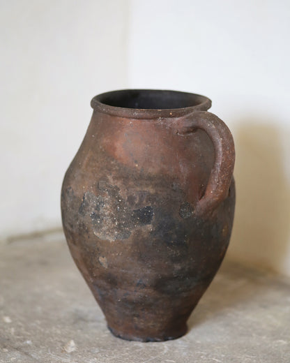 Brown ceramic vase with a handle on a light background