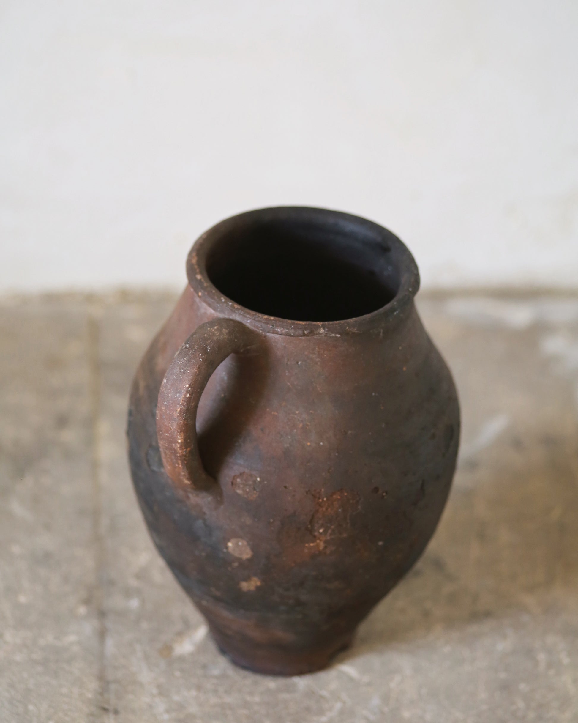 Antique Brown clay pitcher pot vase with a handle on a stone surface