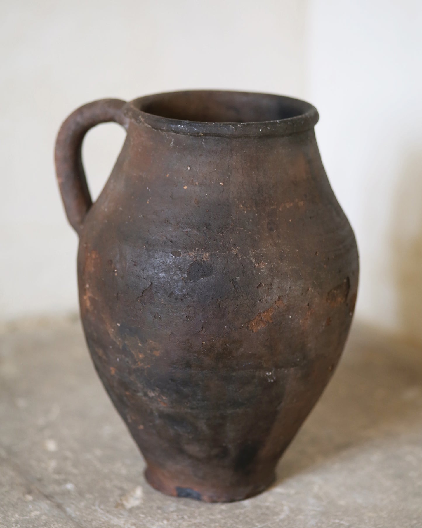 Brown ceramic jar with a handle on a light background