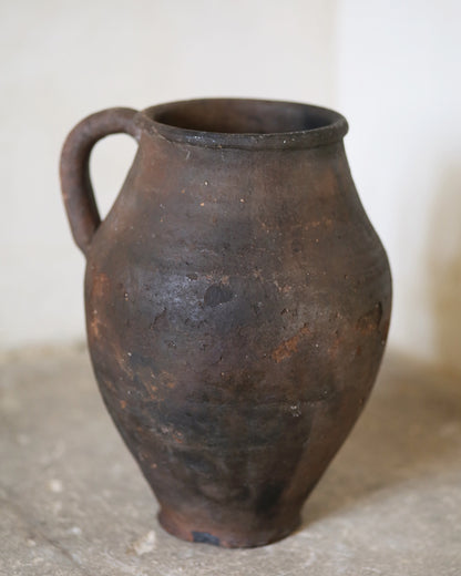 Brown ceramic jar with a handle on a light background