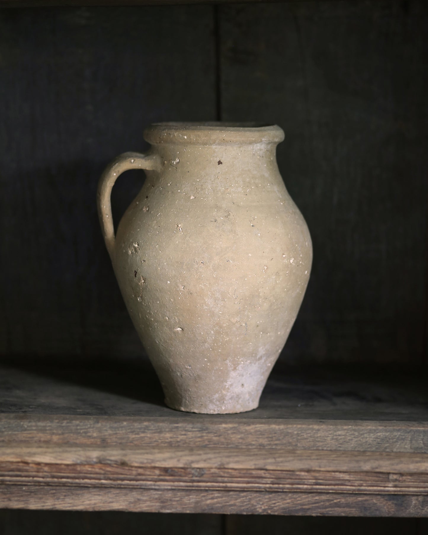 Beige ceramic jar on a wooden shelf with a dark background